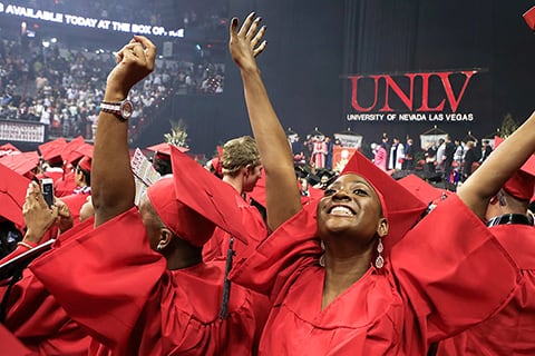 Female graduate raises her hands up in celebration during commencement